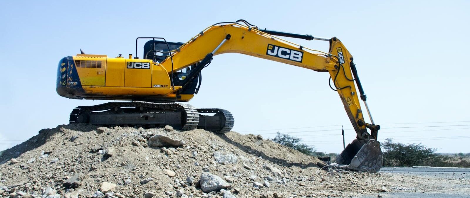 Yellow excavator on a pile of dirt at a construction site under clear blue sky.